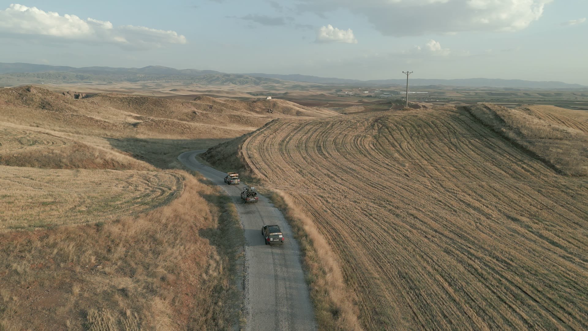 Rally vehicles on a road winding through the Anatolian highlands at golden hour